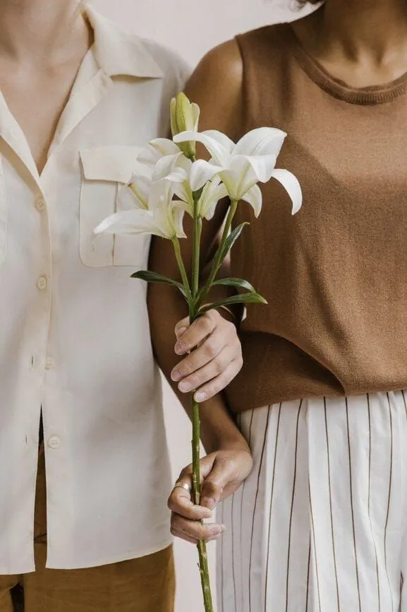 Duas mulheres lado a lado, uma delas segurando um lírio branco, simbolizando as fases da vida da mulher