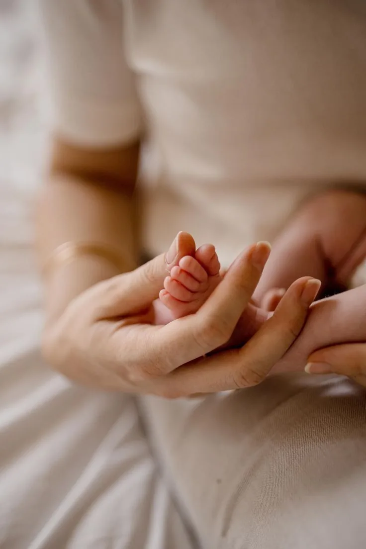 Mãos de uma mulher segurando com carinho o pezinho de um bebê